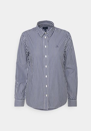 Chemise à manches longues à boutons avec rayures verticales bleu marine et blanches, col classique, présentée sur un fond uni.