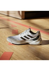 Białe buty sportowe z czarnymi akcentami, z teksturowaną siateczkową cholewką, wyraźnym logo w postaci trzech pasków oraz solidną gumową podeszwą.