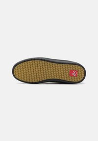 Black shoe sole with a textured gum rubber outsole featuring a herringbone pattern and a red logo accent. Flat, rounded edges.