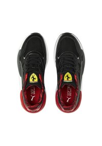 Zapatillas negras con parte superior texturizada, acentos rojos y un logo amarillo en la lengüeta. Suela blanca con interior acolchado.