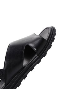 Sandalo in pelle nera con una fascia ampia, punta aperta, finitura testurizzata e suola in gomma resistente caratterizzata da un modello di battistrada robusto.