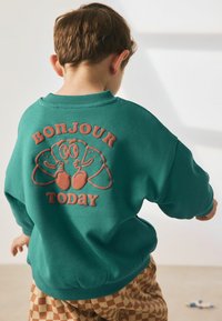 Sweatshirt teal cu guler rotund, având o grafică ridicată de culoare portocalie cu croissante în stil desenat și textul „BONJOUR TODAY” pe spate.