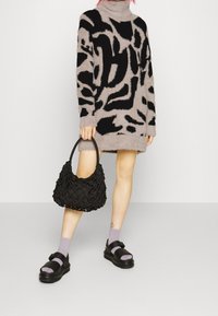 Maglione fuzzy nero e beige con motivo astratto, abbinato a una borsa nera testurizzata e sandali neri sopra calzini lavanda.