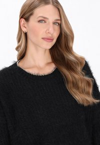 Czarny puszysty sweter z okrągłym dekoltem i teksturowanym wzorem. Posiada srebrny akcent wzdłuż dekoltu. Miękki, ciepły materiał.