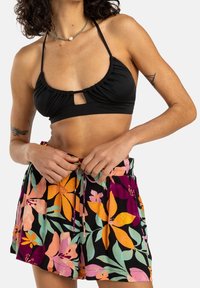 Sort bikini-top med rynket detalje og nøglehul, kombineret med flerfarvede blomstrede shorts med orange, pink og grønne accenter.