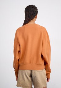 Orange sweatshirt med rund halsudskæring, ribbede manchetter og kant, samt en afslappet pasform. Sammen med beige shorts, der har et struktureret stof.