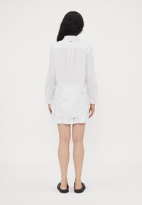 Camicia bianca a maniche lunghe con colletto button-down, dotata di yoke posteriore e spacchi laterali, realizzata in tessuto leggero e dalla consistenza liscia.