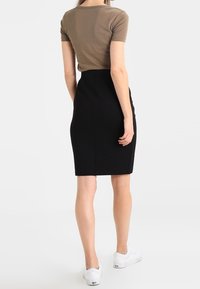 Form-fitting black pencil skirt paired with a short-sleeve brown top. Model wears white sneakers. Smooth texture and clean lines.