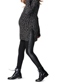 Pull de maternité en tricot noir et blanc avec des fentes sur les côtés, associé à un legging noir avec des panneaux en simili cuir et des bottines noires.