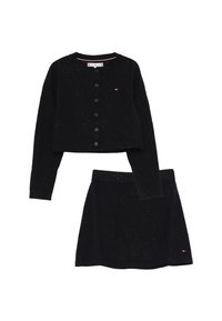 Cardigan nero a maglia con bottoni e gonna coordinata, entrambi punteggiati di pois bianchi e con piccoli loghi del marchio sul petto e sull'orlo della gonna.