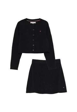 Cardigan nero a maglia con bottoni e gonna coordinata, entrambi punteggiati di pois bianchi e con piccoli loghi del marchio sul petto e sull'orlo della gonna.