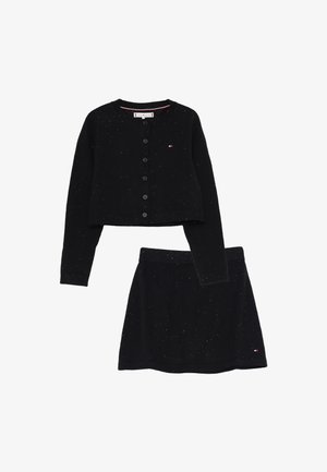 Cardigan nero a maglia con bottoni e gonna coordinata, entrambi punteggiati di pois bianchi e con piccoli loghi del marchio sul petto e sull'orlo della gonna.