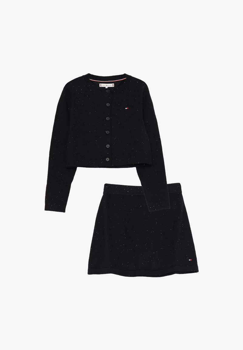 Cardigan nero a maglia con bottoni e gonna coordinata, entrambi punteggiati di pois bianchi e con piccoli loghi del marchio sul petto e sull'orlo della gonna.