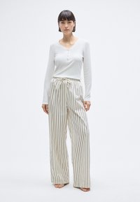 Haut blanc à manches longues avec détail de boutons, associé à un pantalon large crème à rayures, muni d'une taille à cordon.