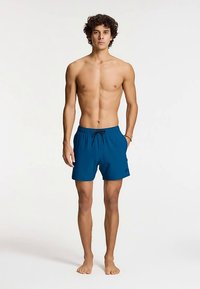 Plave kupaće hlače od lagane tkanine s elastičnim pojasom i vezicom. Dizajn je jednostavan s jednim malim logotipom.