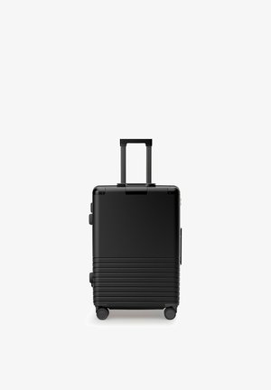 Valise cabine rigide noire avec poignée télescopique déployée et quatre roues pivotantes sur fond blanc.