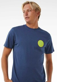 Camiseta de algodón azul marino con mangas cortas que presenta un logo circular amarillo en el área izquierda del pecho. Textura suave y corte estándar.