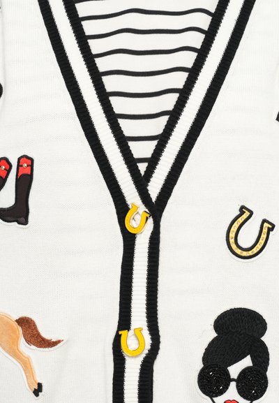Cardigan bianco con rifiniture nere, caratterizzato da un motivo a righe, icone ricamate che includono ferri di cavallo, stivali e un volto stilizzato con occhiali da sole.