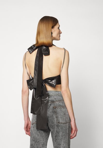 Black backless top with a large bow at the back, chain straps, and smooth texture; paired with high-waisted gray denim jeans.