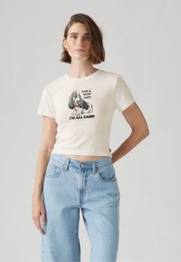 Vit bomullstopp med korta ärmar, med en tryckt grafisk bild av en hund och texten "HAD A RUFF DAY? I'M ALL EARS!" i svart. Ljust blå denimjeans.