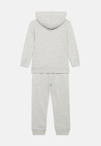 Hanorac cu glugă din bumbac gri și pantaloni de trening asortați. Materialul este moale și texturat, cu manșete ribbate. Design simplu, fără modele sau accente.