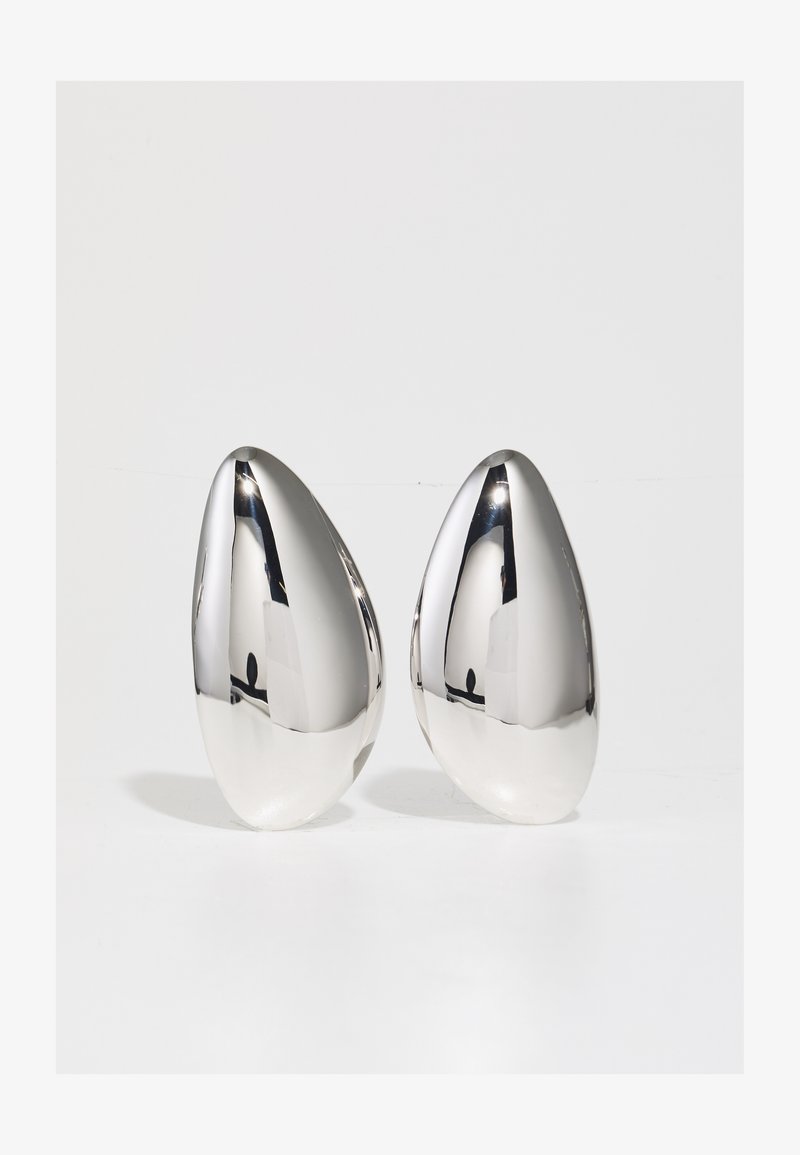 Dwa dekoracyjne elementy metaliczne w kolorze srebrnym, w kształcie kropli, o gładkiej, lustrzanej powierzchni i matowej podstawie w kontrastującym kolorze.