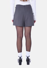 Pantaloni corti grigi sartoriali con vita alta, chiusura con zip sul retro e design plissettato. Le calze e le scarpe nere con tacco completano l'outfit.