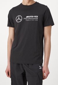Czarna bawełniana koszulka z białym logo zespołu AMG Petronas Formula One Team na piersi. Krótkie rękawy i klasyczny okrągły dekolt.