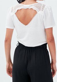 Witte t-shirt met korte puffmouwen en een kanten rugdetail met een V-hals. Gecombineerd met elastische zwarte broeken voor een casual look.