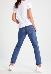 Lightweight white t-shirt with short sleeves, paired with blue jeans featuring a straight fit and detailed back pockets. Worn with white sneakers.