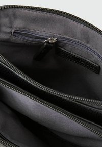 Das Innere des schwarzen Leder-Reißverschlussbeutels verfügt über eine glatte Stoffauskleidung, eine kleine Reißverschlusstasche und sichtbare Nähte, die organisierte Fächer schaffen.