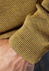 Knit sweater cuff in yellow with a textured mesh pattern, featuring ribbed detailing at the edge and contrasting black accents.