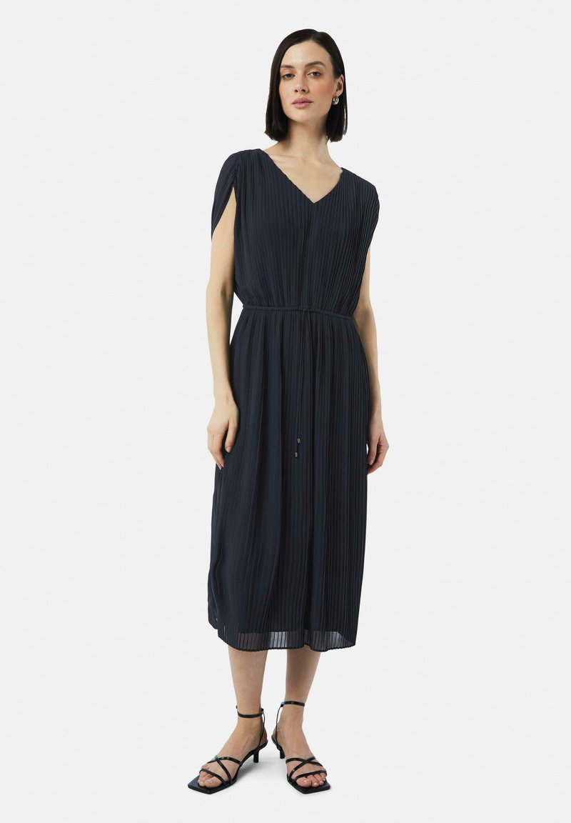 Navy-blaues plissiertes Kleid mit V-Ausschnitt und kurzen, drapierten Ärmeln, tailliert in der Taille. Kombiniert mit schwarzen, geschnürten High Heels. Weicher Stoff.
