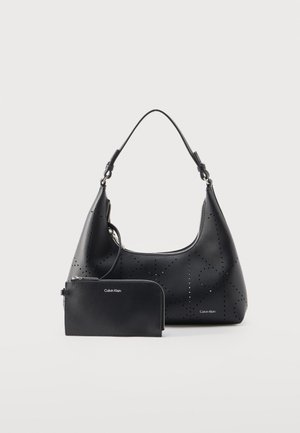Črna usnjena torbica za čez ramo s perforiranim vzorcem in ujemajočim se denarnico z zadrgo, obe z napisom »Calvin Klein« v srebrnih črkah.