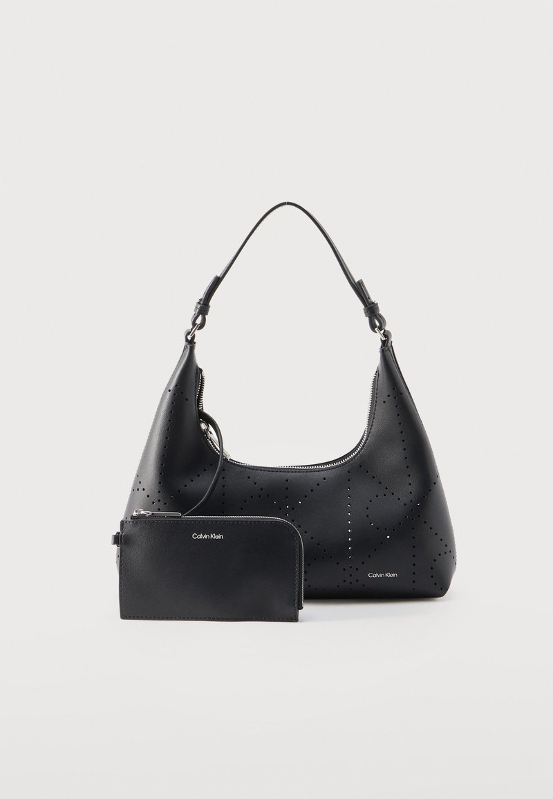 Μαύρη δερμάτινη τσάντα ώμου με διάτρητο σχέδιο και ταιριαστό πορτοφόλι με φερμουάρ, και τα δύο με το λογότυπο "Calvin Klein" σε ασημένια γράμματα.
