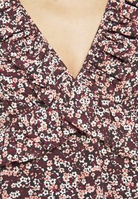 Gros plan d'une robe fleurie avec de petites fleurs roses et blanches sur un fond sombre, avec des détails froncés le long d'un décolleté en V.