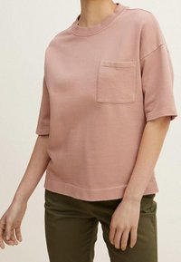 Dammrosa t-shirt med kort ärm i mjukt material, med rund hals och en bröstficka; matchad med olivgröna byxor.