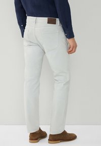 Jeans gris claro de corte ajustado, con bolsillos traseros y un parche de cuero marrón en la cintura. Completos con zapatos de ante marrón.