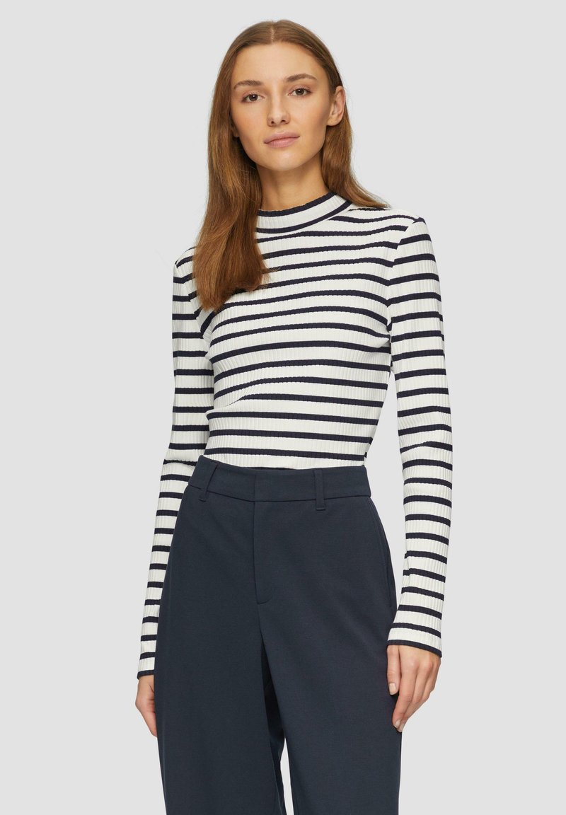 Top a maniche lunghe a coste con righe verticali blu navy e bianche, collo alto e silhouette aderente, abbinato a pantaloni scuri a vita alta.