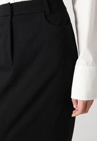 Pantaloni negri, ajustați, cu o textură netedă, având un detaliu de buzunar lateral și un talie plată, asortați cu un manșon de cămașă albă.