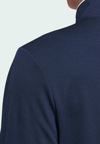 Tummansininen takki, jossa on teksturoitu kangas, korkea kaulus ja muotoillut hartiat, mikä antaa räätälöidyn ilmeen.