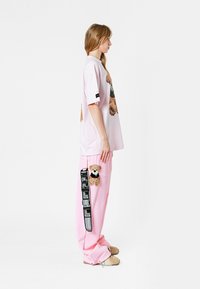 Camiseta rosa de gran tamaño con diseño floral; pantalones rosa sueltos con parche de oso de peluche y detalle de tiras negras. Modelo de pie de lado.