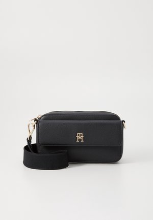 Sac bandoulière rectangulaire en cuir noir avec plaque logo dorée, fermeture éclair sur le dessus, poche avant à rabat et sangle en tissu réglable.
