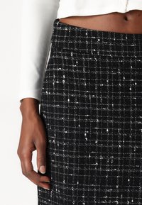 Jupe à carreaux noir et blanc en tissu texturé, dotée d'une taille ajustée, avec des coutures visibles et une finition lisse.