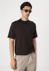 Svart bomull t-skjorte med rund hals og korte ermer, kombinert med lyse beige bukser. Stoffet ser glatt og uten dekorasjoner ut.