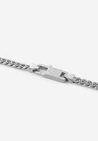 Bracelet en chaîne argentée avec des maillons interdépendants, un fermoir texturé au motif en diamants et une gravure de marque.
