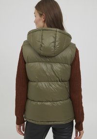 Gilet matelassé vert olive avec capuche, présentant une texture brillante et un design matelassé horizontal, associé à une manche en tricot marron côtelé.