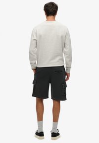 Sudadera gris de manga larga, combinada con pantalones cortos cargo oscuros que tienen múltiples bolsillos laterales. Zapatillas negras y calcetines grises completan el look.