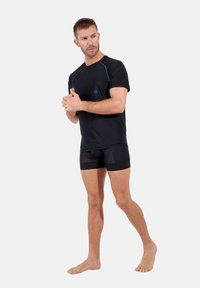 Svart atletisk t-shirt med blå accenter och logotyp, i kombination med svarta åtsittande shorts med nätpaneler. Modellen står barfota.