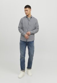 Camisa de cuadros en blanco y negro, con cuello y mangas largas, combinada con unos vaqueros azules y zapatillas blancas.